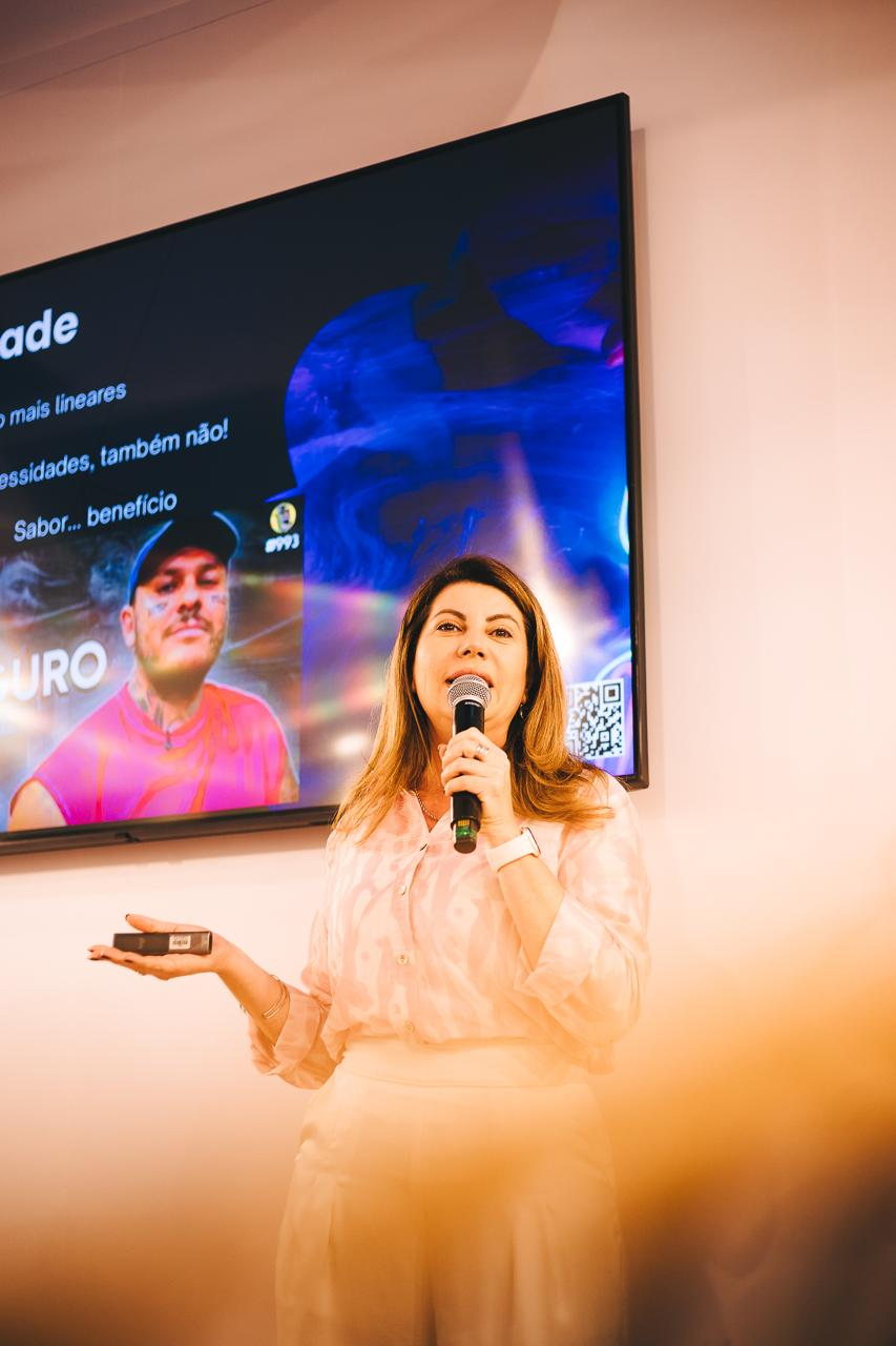 Patrícia Rodrigues conduzindo uma apresentação de palco, com microfone em uma das mãos e apresentador na outra.