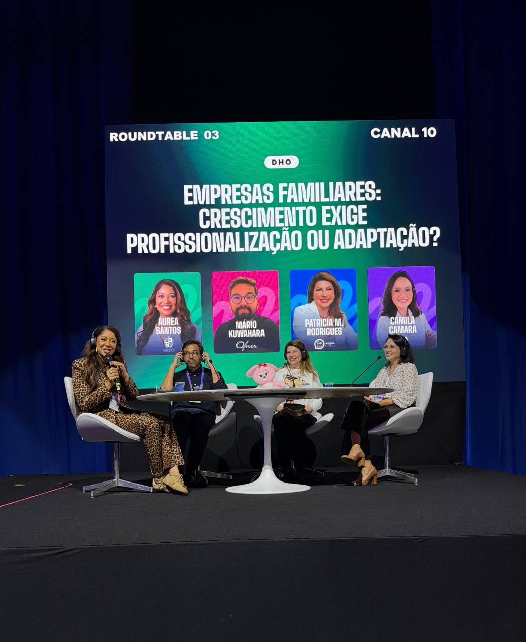 Patrícia Rodrigues participando de uma mesa de debate no palco, sentada com outros convidados durante a conversa.